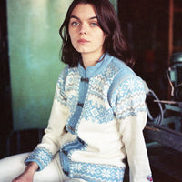Person wearing a white and blue patterned sweater sitting indoors.