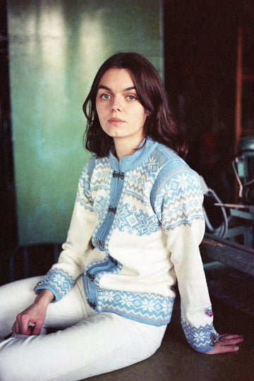 Person wearing a white and blue patterned sweater sitting indoors.