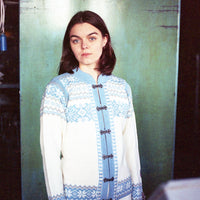 Person wearing a blue and white patterned cardigan against a green wall.