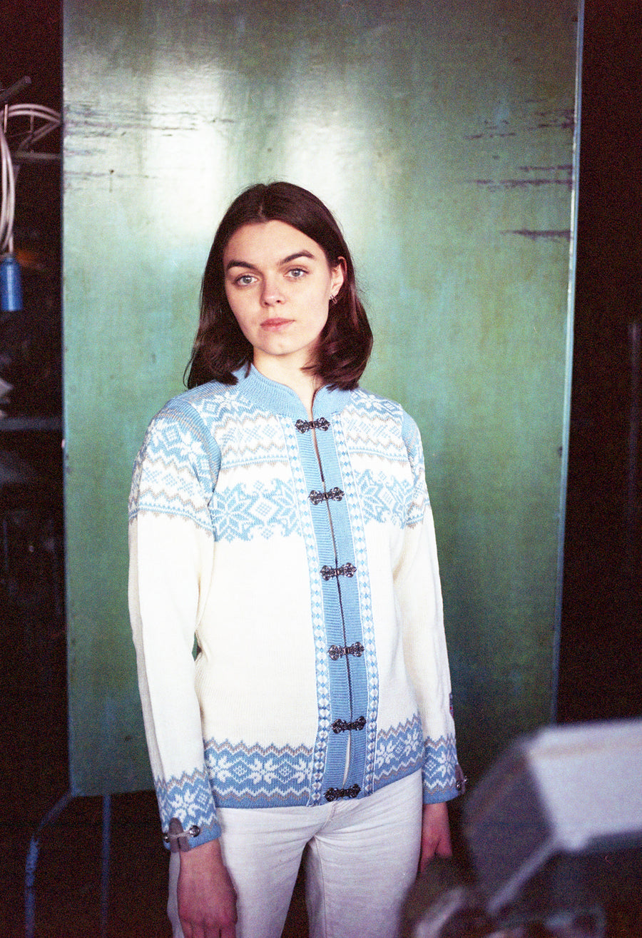 Person wearing a blue and white patterned cardigan against a green wall.