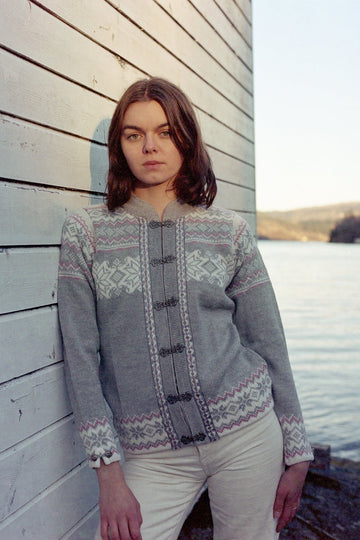 Model wears the Voss cardigan in Grey and leans against a wooden wall.