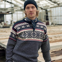 Man wearing a patterned sweater and beanie standing in a greenhouse.