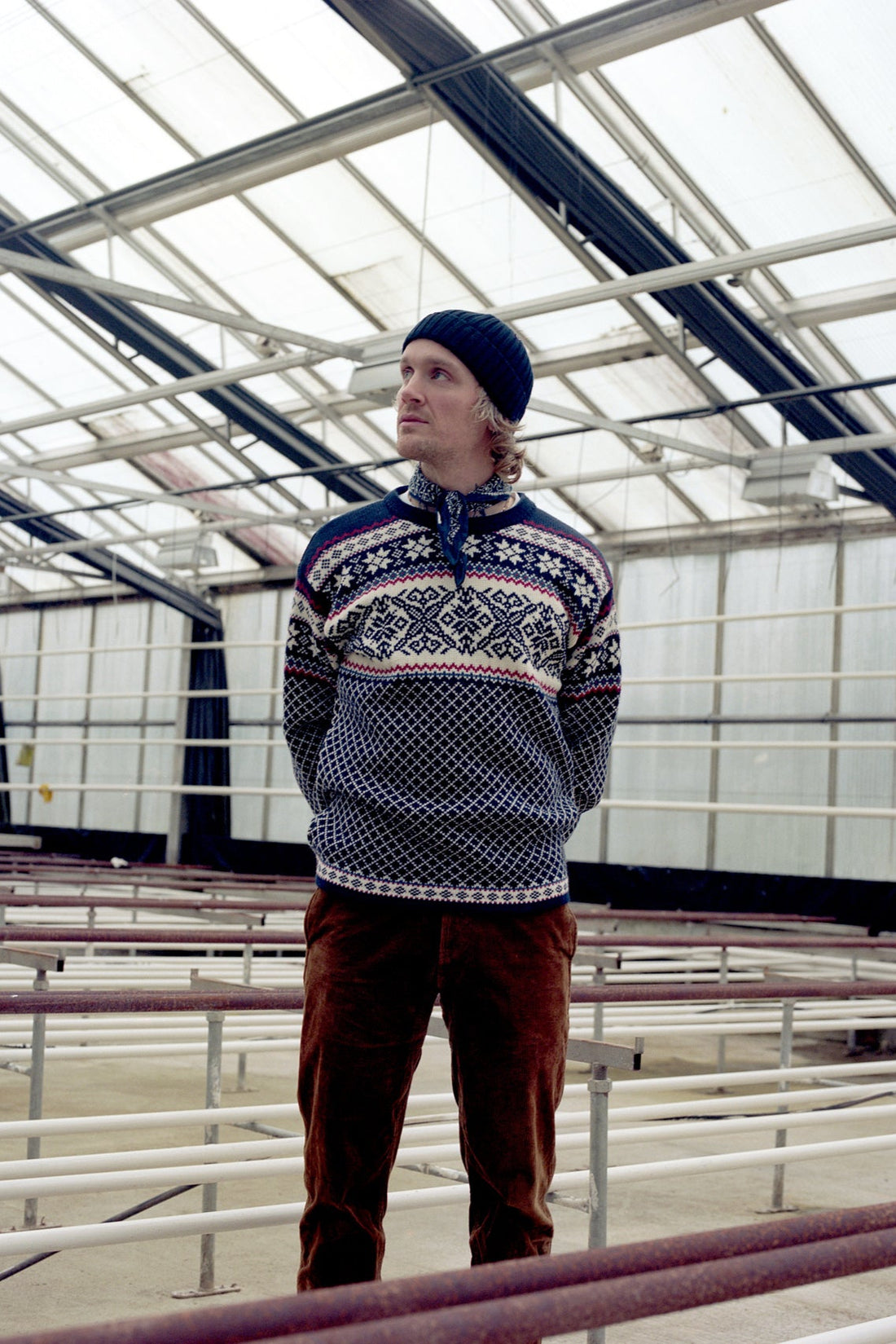 Person wearing a patterned sweater and beanie standing inside a large industrial building.