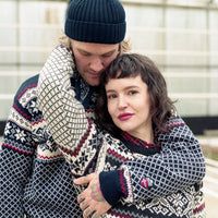 Two people wearing matching patterned sweaters and hats in an indoor setting.
