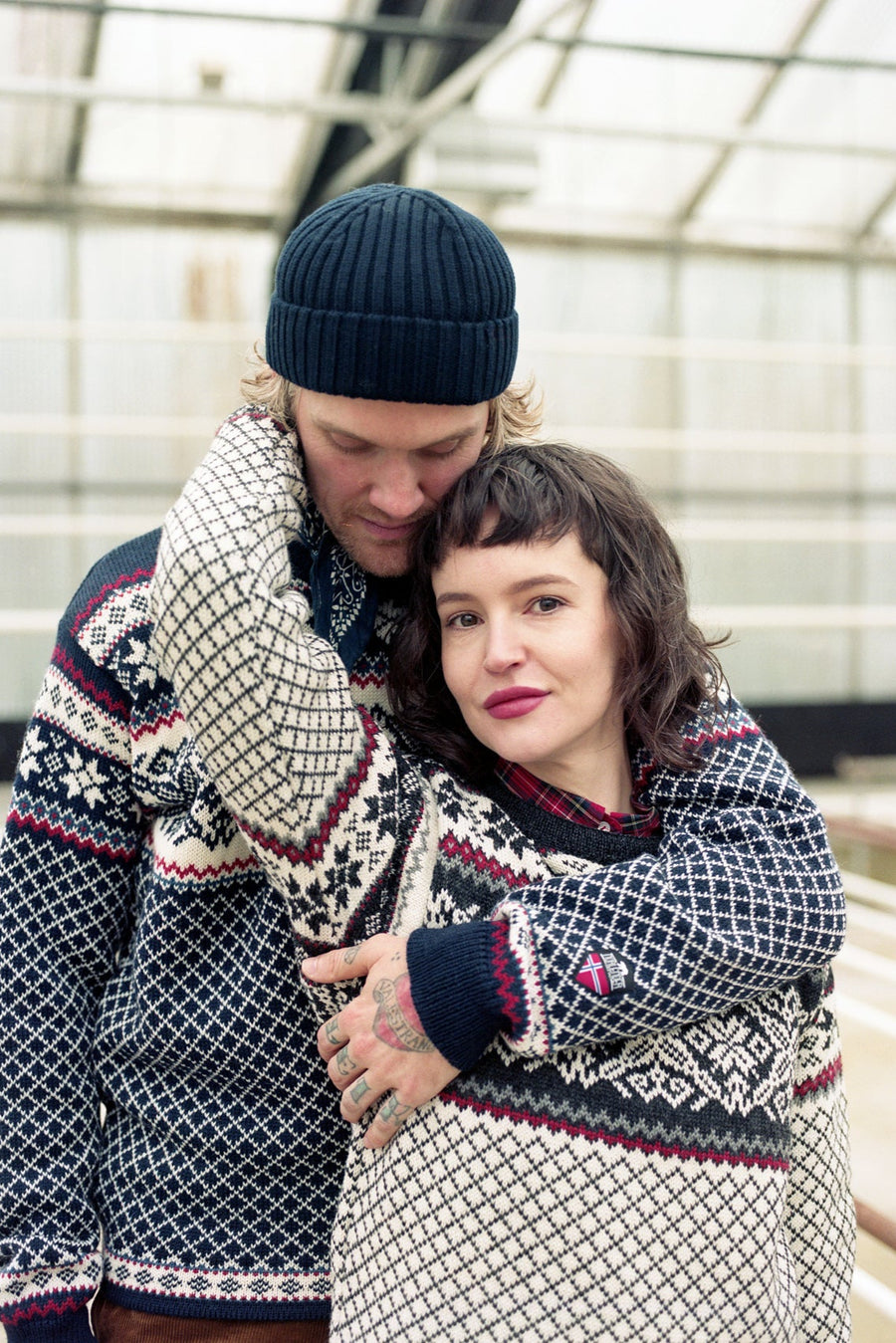 Two people wearing matching patterned sweaters and hats in an indoor setting.