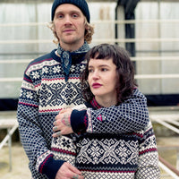 Two people wearing matching patterned sweaters in an indoor setting.