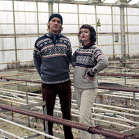 Two people wearing matching patterned sweaters in a greenhouse setting.