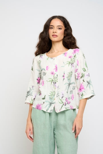 Woman wearing a floral blouse and light green pants against a white background