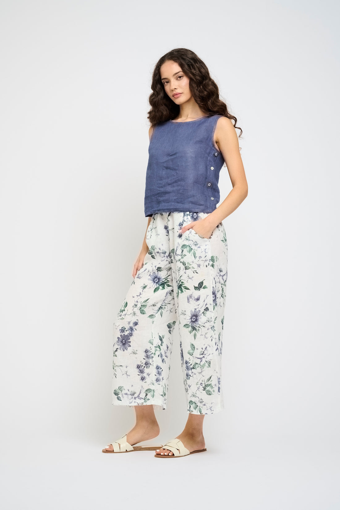 Woman wearing a blue sleeveless top and floral pants on a white background