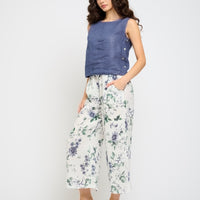 Woman wearing a blue sleeveless top and floral pants on a white background