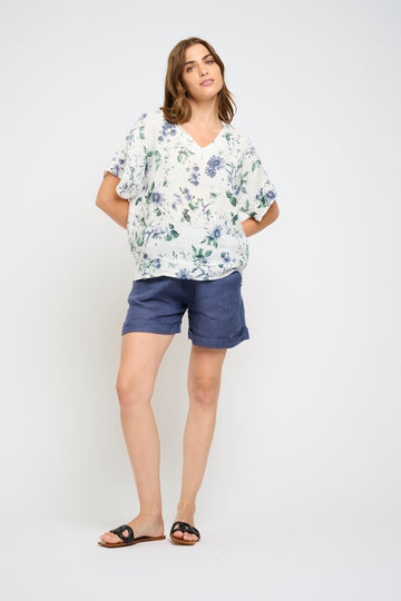 Woman wearing a floral blouse and blue shorts on a white background