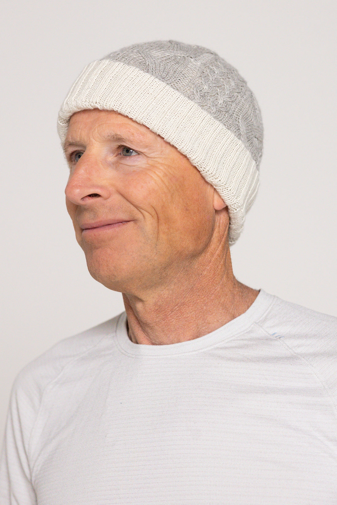 Person wearing a gray knit beanie and white shirt against a plain background
