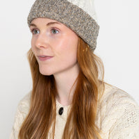 A person wearing a reversible beanie with one side tricolour and the other side white with a textured pattern.