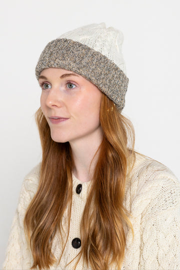 A person wearing a reversible beanie with one side tricolour and the other side white with a textured pattern.