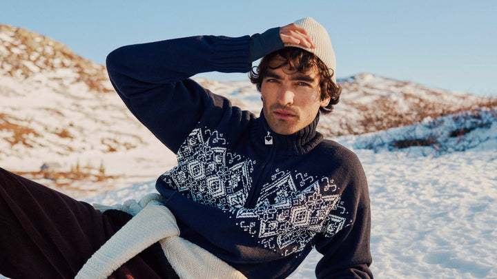 Man wearing a patterned sweater and cap sitting in a snowy landscape
