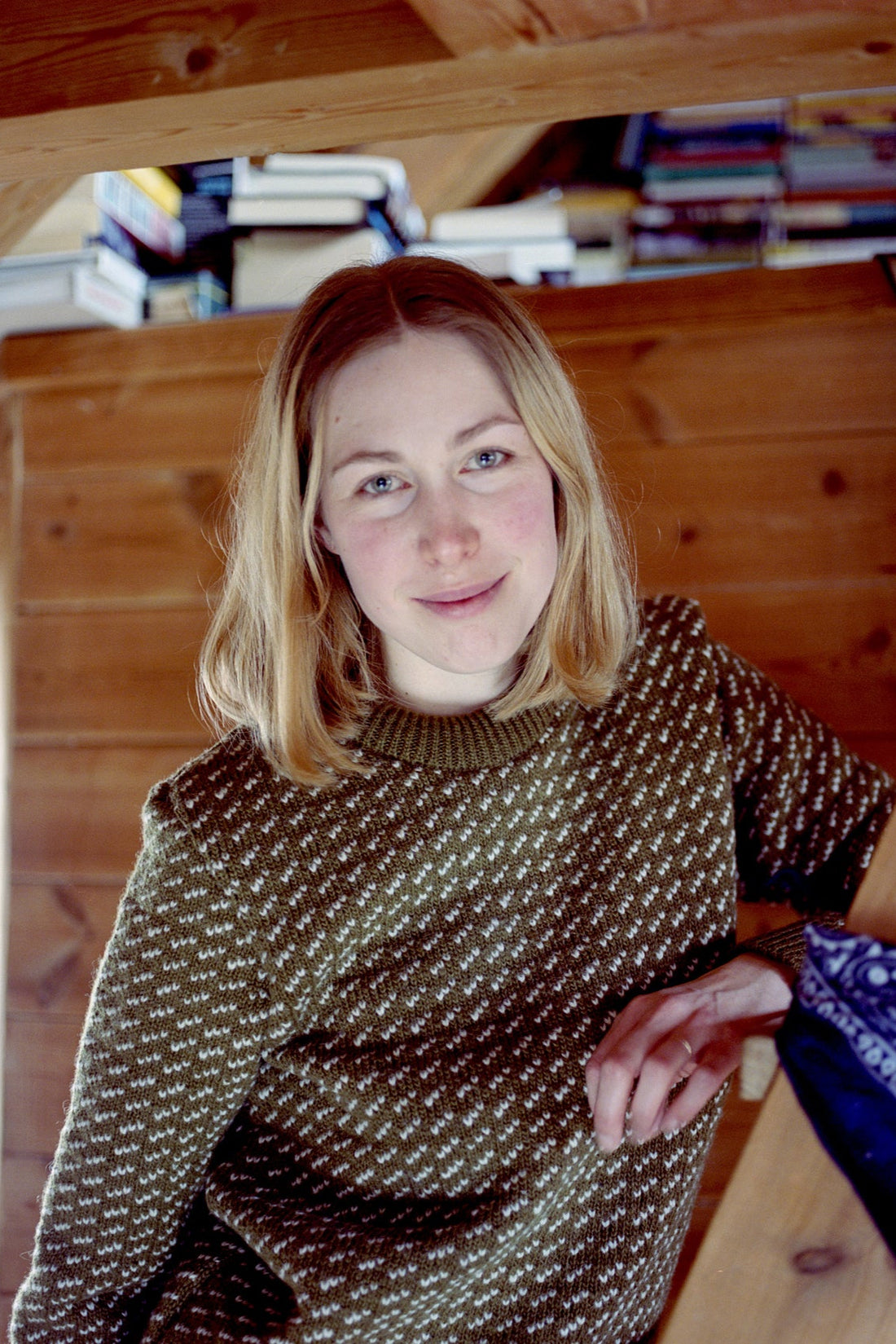 Woman wearing a patterned sweater indoors with wooden walls and books in the background