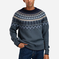 Man wearing a patterned sweater and jeans on a white background