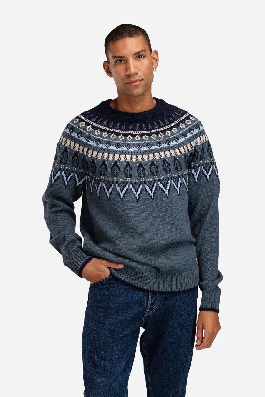 Man wearing a patterned sweater and jeans on a white background