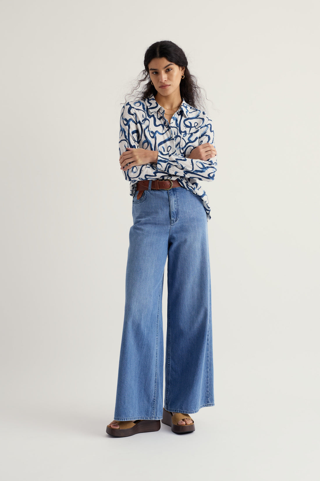 Woman wearing a patterned shirt and blue jeans on a plain background