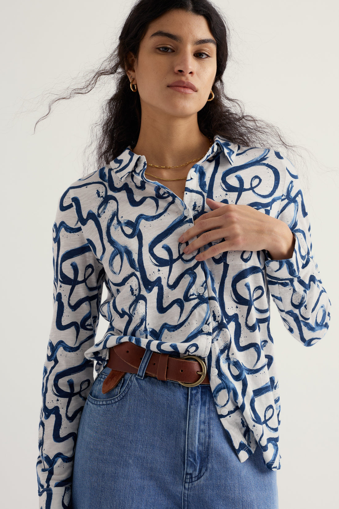Woman wearing a blue and white patterned shirt with blue jeans on a white background