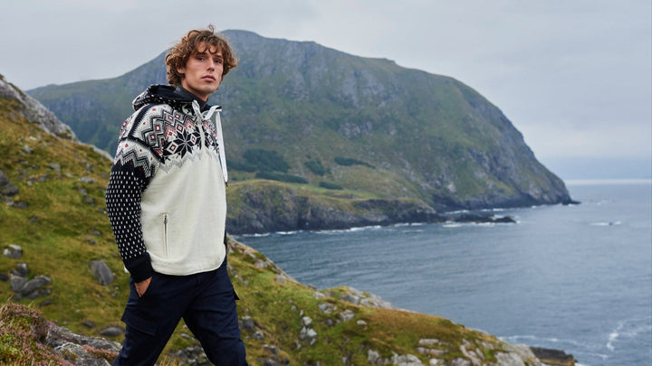 Person standing on a grassy cliff overlooking the ocean with mountains in the background
