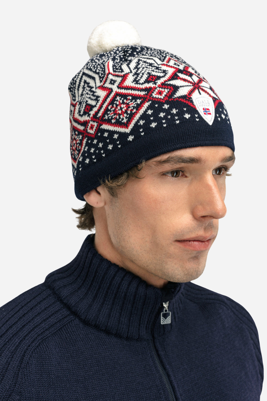 Man wearing a patterned beanie with a white pom-pom on a white background