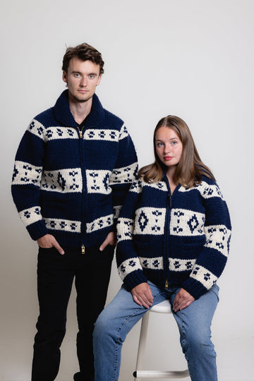 Two people wearing matching navy blue sweaters with white patterns on a plain background