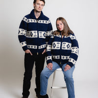 Two people wearing matching navy and white patterned sweaters on a white background