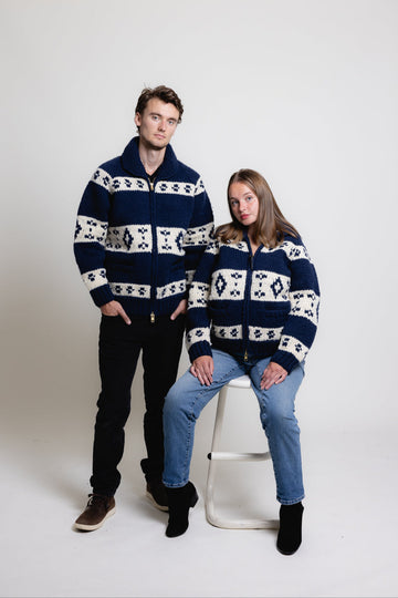 Two people wearing matching navy and white patterned sweaters on a white background
