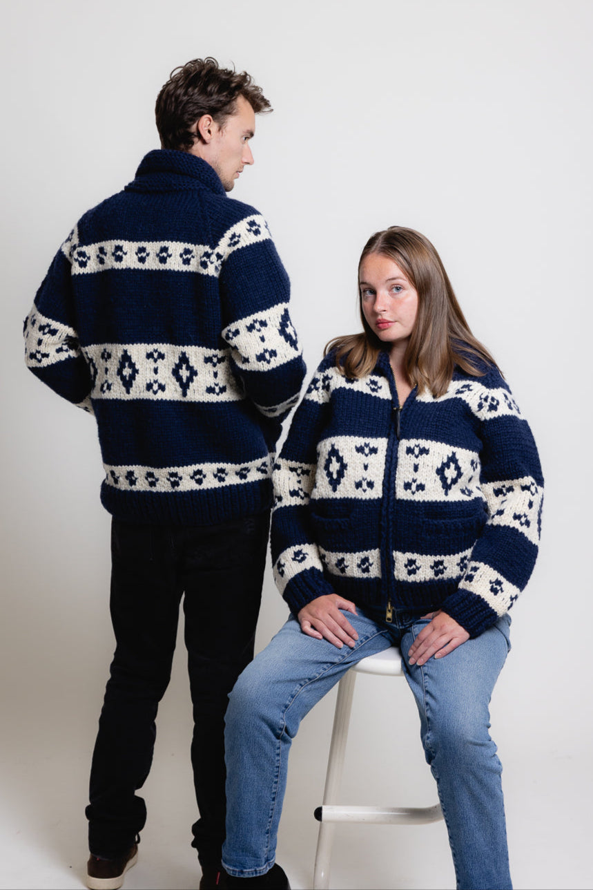 Two people wearing matching navy blue sweaters with white patterns on a white background