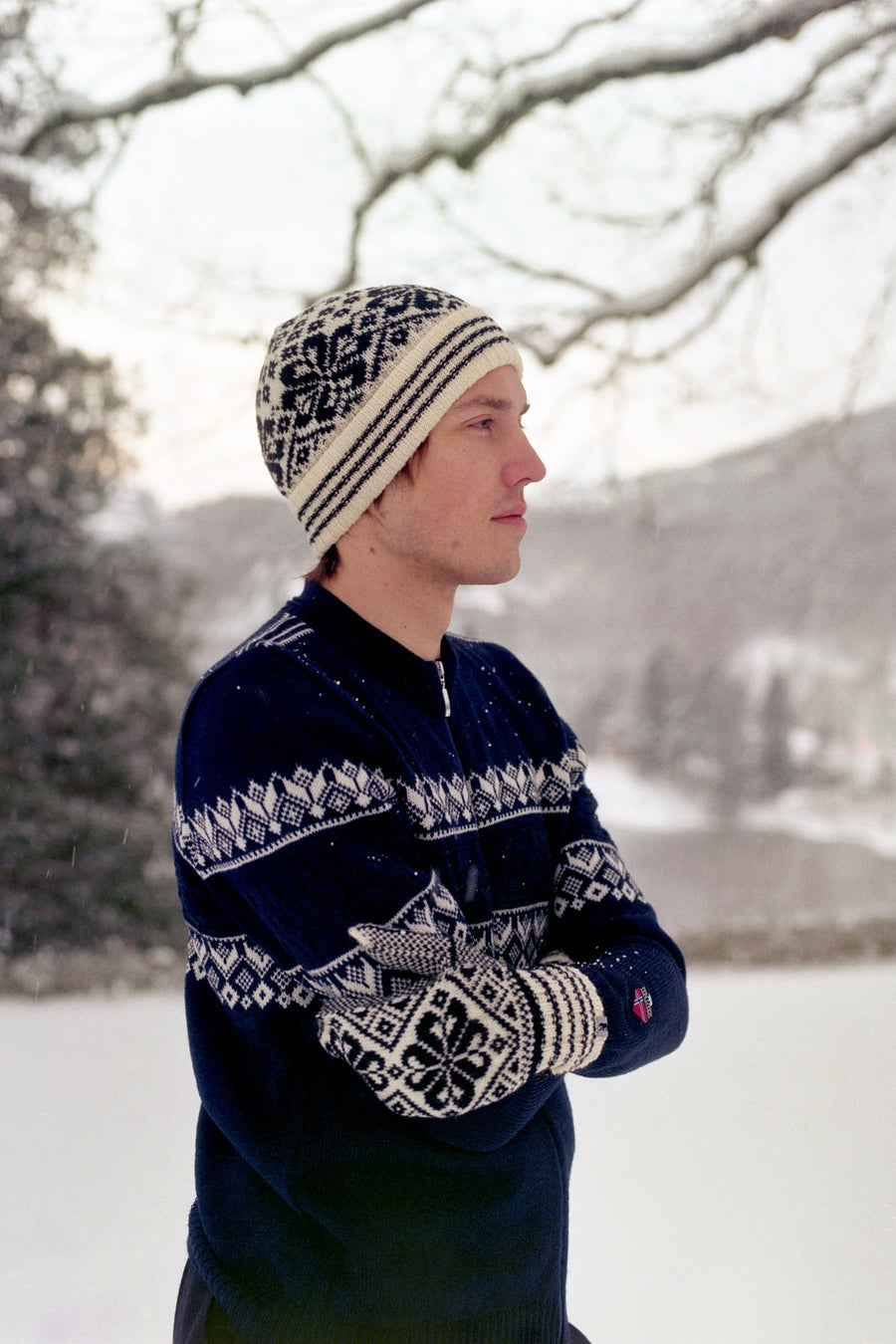 Person wearing a patterned knit sweater and hat in a snowy landscape