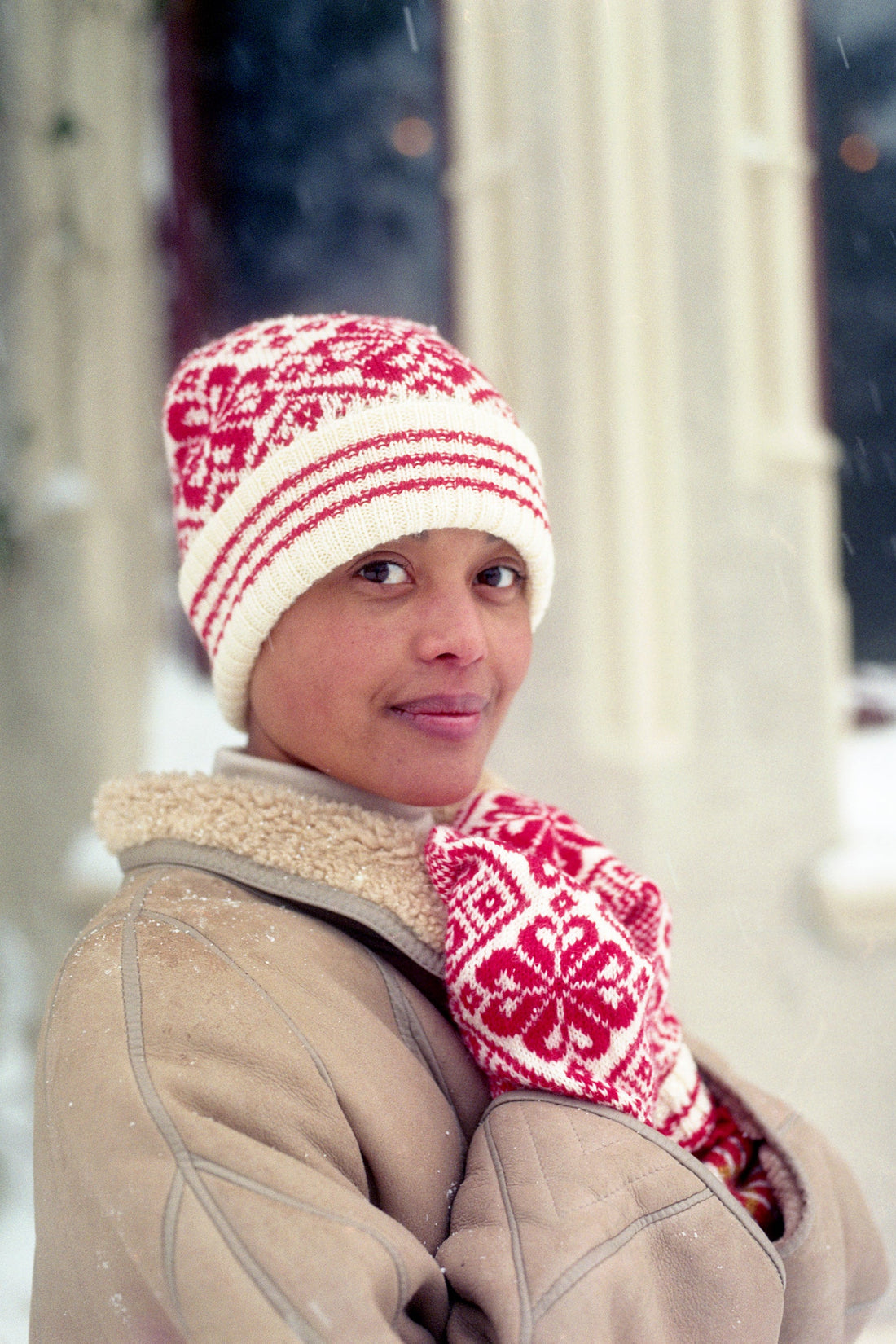 Person wearing a red and white patterned knit hat and mittens outdoors.