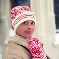 Person wearing a red and white patterned knit hat and mittens outdoors.