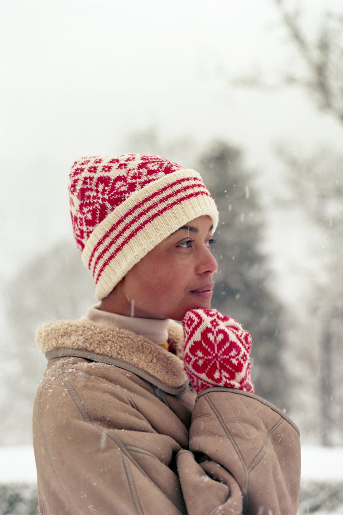 Person wearing a red and white patterned knit hat and mittens in a snowy landscape